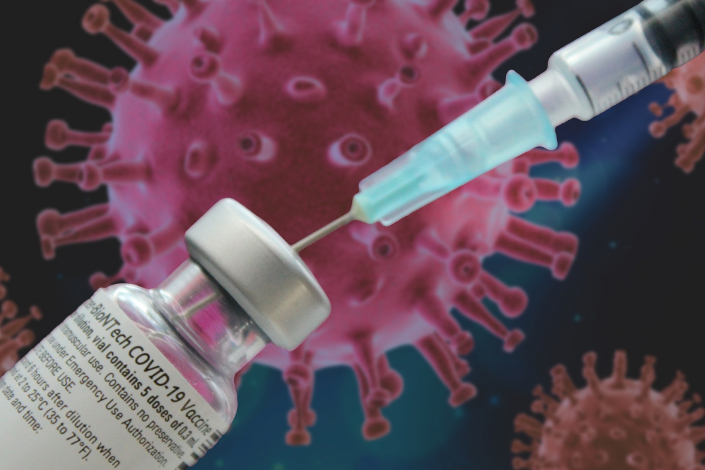 Spritze mit BionTech-Impfdosis vor einem Coronavirus